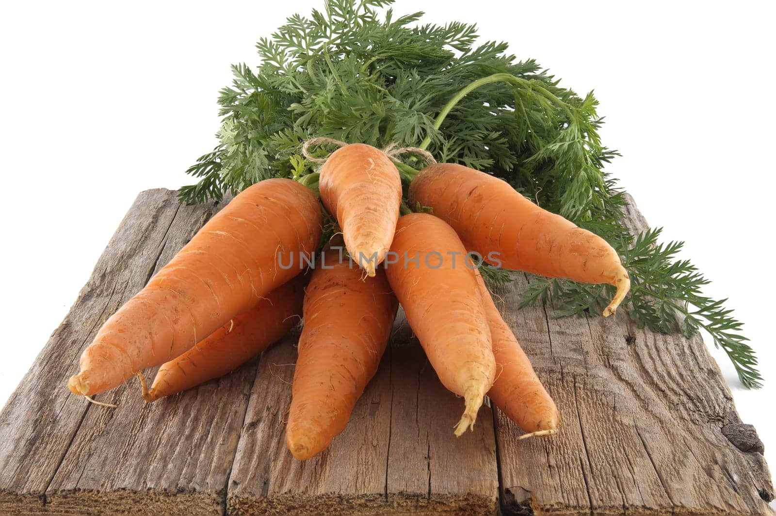 Bunch of fresh, orange carrots with green tops is neatly tied together using twine and positioned on an old, rustic wooden table