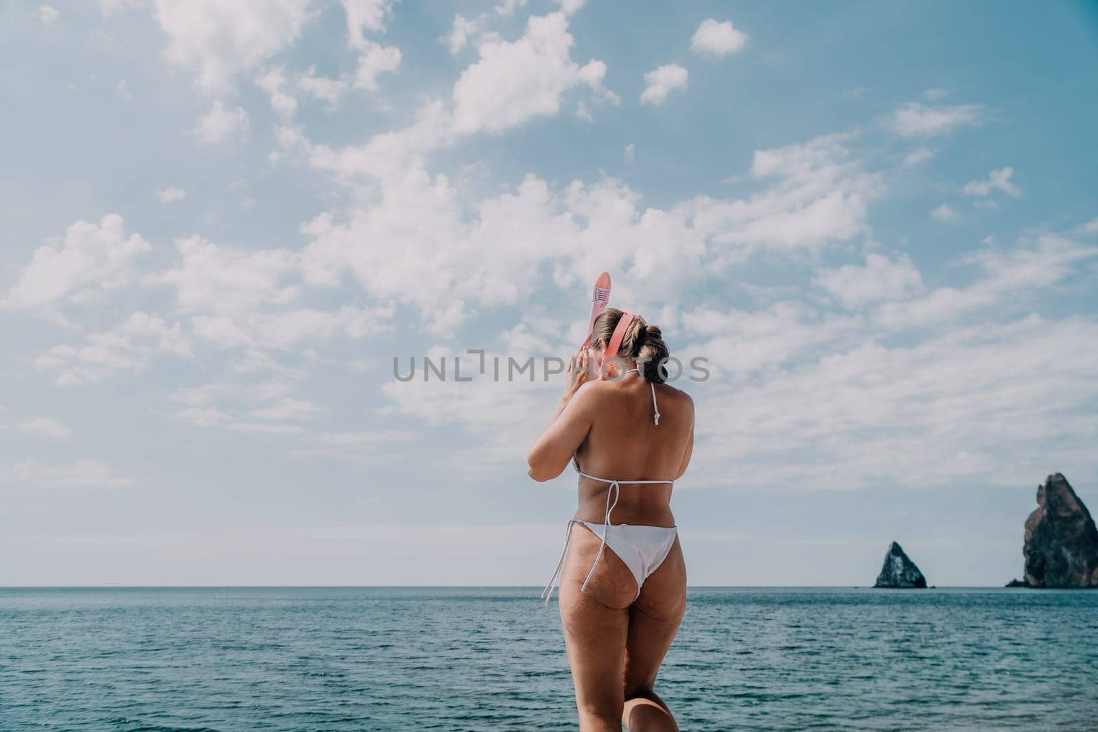 Young happy woman in white bikini put pink snorkeling mask on beach before swimming. girl having fun relaxing on beautiful beach. Beach lifestyle