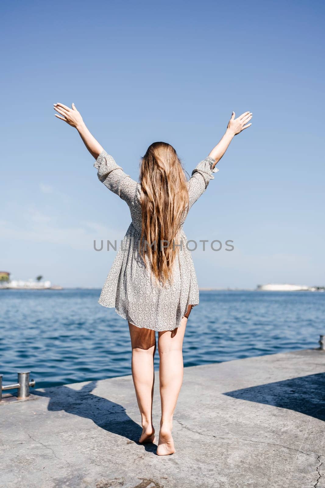 woman in a dress stands on a dock by the water, her arms raised in the air. Concept of freedom and joy, as the woman is celebrating or expressing her happiness. by Matiunina