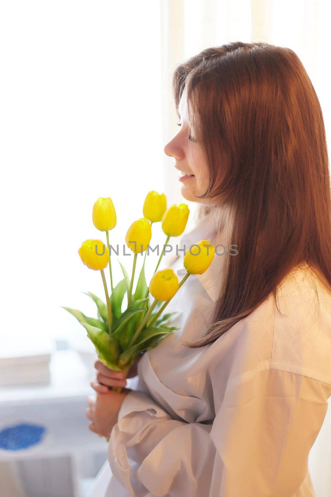 Beautiful sweet girl in nightgown in early morning with bouquet of delicate yellow tulips. Gift on International Women's Day on March 8th. Cosmetics, skin and hair care. Perfume, natural fragrance