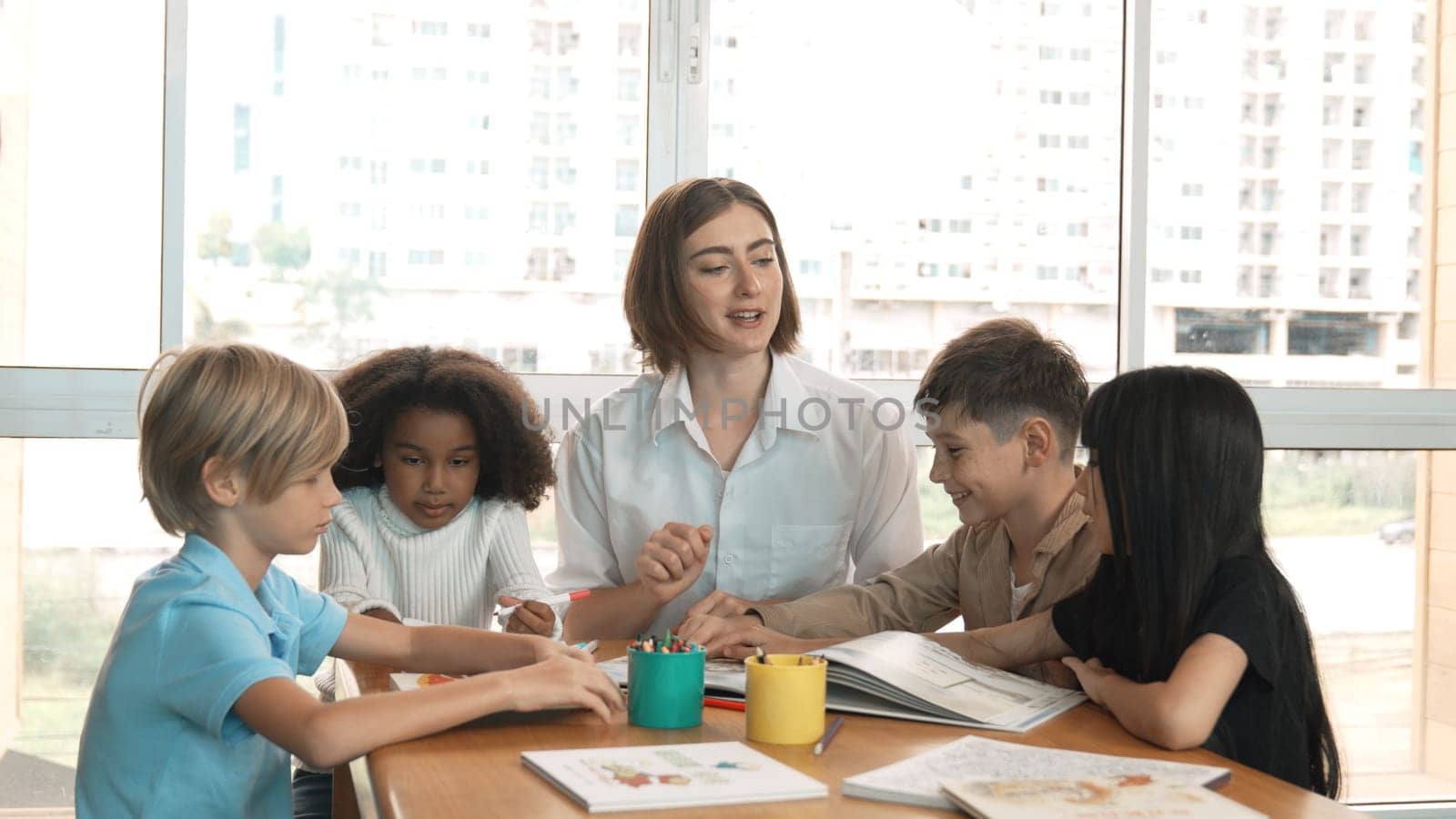 Happy diverse student and smart teacher drawing and coloring by using marker at drawing book. Multicultural smart learner using drawing book while talking to skilled caucasian instructor. Erudition.