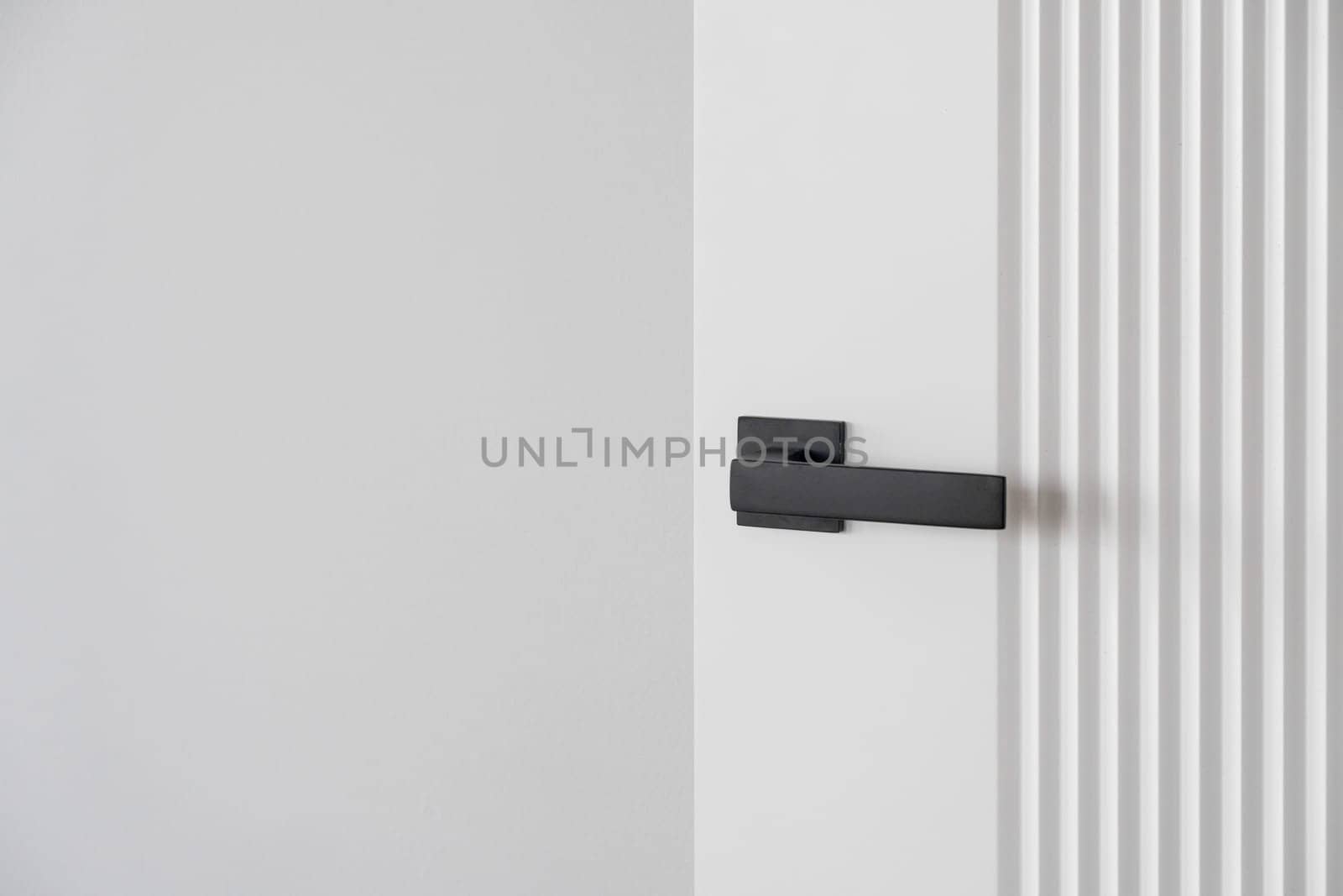 Modern black door handle on white wooden door in interior. by AnatoliiFoto