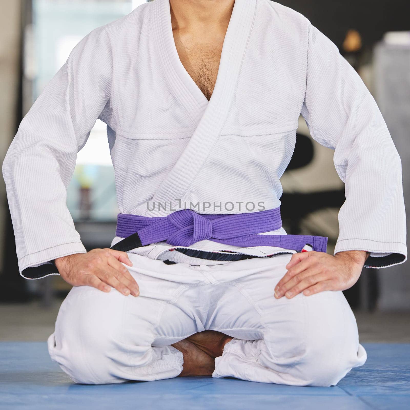Martial arts, fitness and man kneeling in gym for training, uniform or professional fighting sport. Health, wellness and Brazilian jiu jitsu athlete in dojo with gi, ground exercise or sitting on mat by YuriArcurs