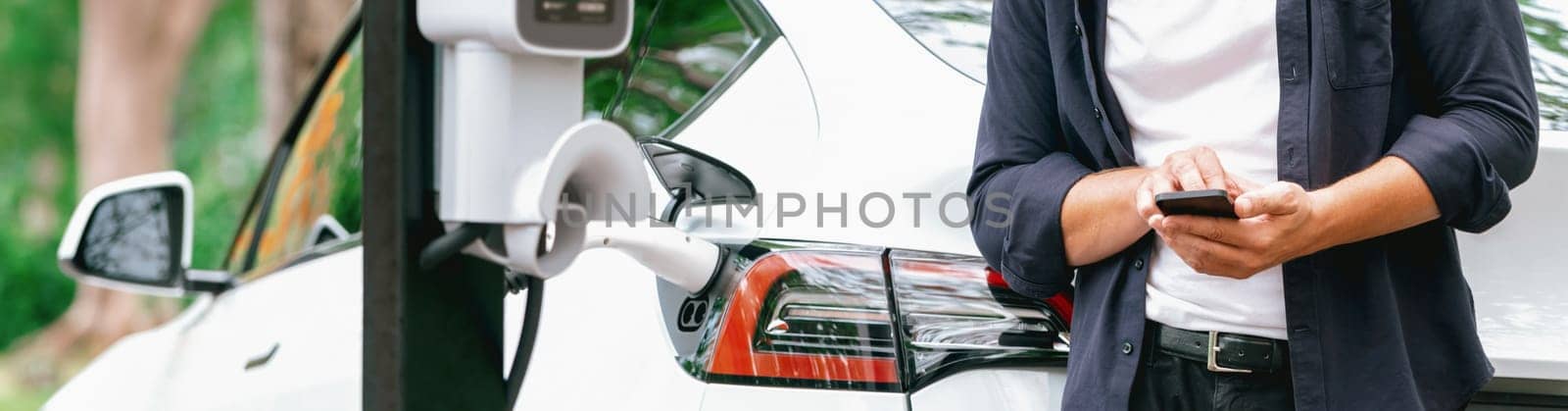 Man using smartphone to pay for electric car charging. Exalt by biancoblue