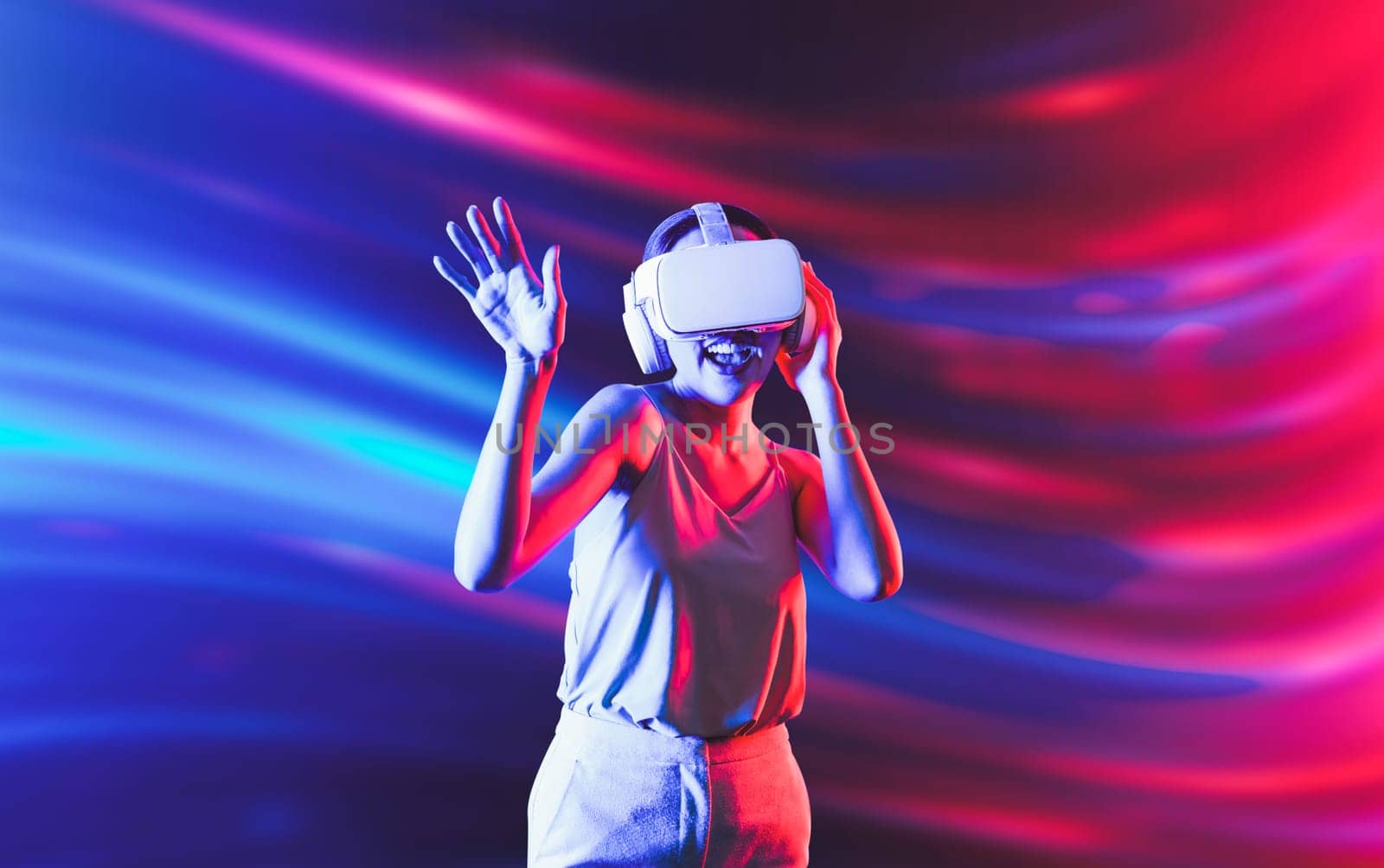 Smart female standing surrounded by neon light wearing VR headset connecting metaverse, future cyberspace community technology. Elegant woman enjoy dancing wavering body and sing song. Hallucination.