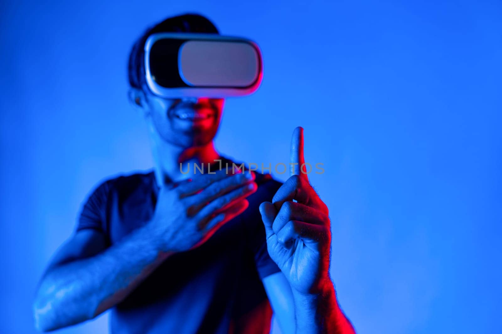 Caucasian man wearing virtual reality goggle while standing at neon light background. Person with VR goggle enter metaverse by using digital futuristic innovation technology while pointing. Deviation.