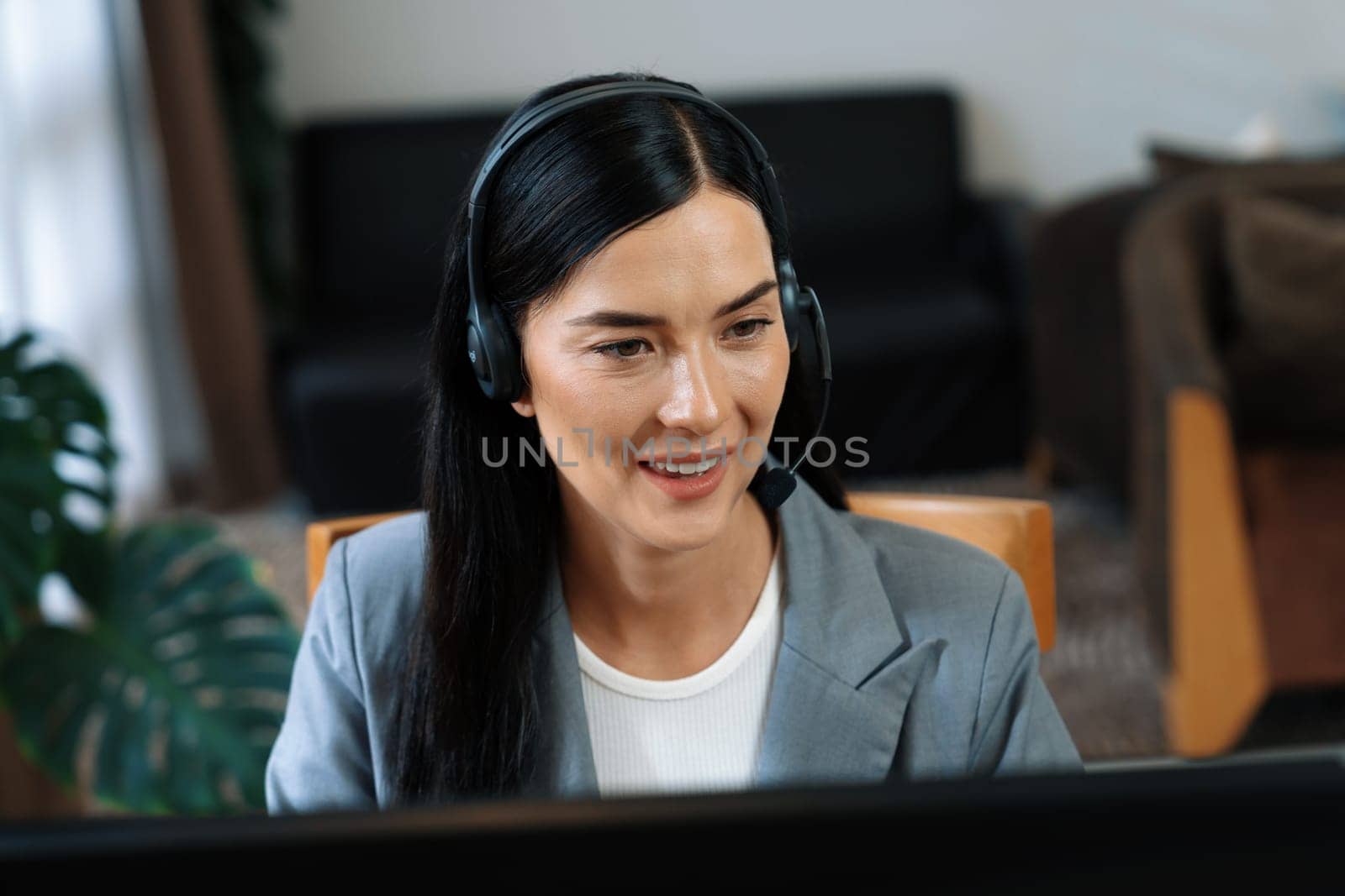 Female call center operator or customer service helpdesk staff working on workspace while talking on the headset to provide assistance for customer. Professional modern business service. Blithe