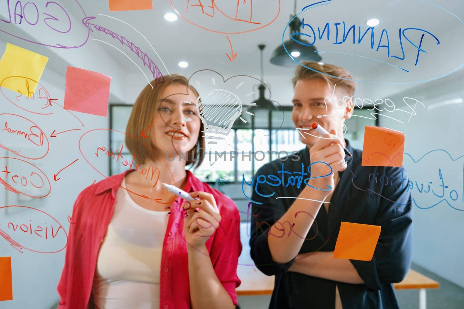 Couple of young creative start up business people brainstorming idea and solving problems by using sticky note and mind map at glass board, meeting room. discussing, working together. Immaculate.