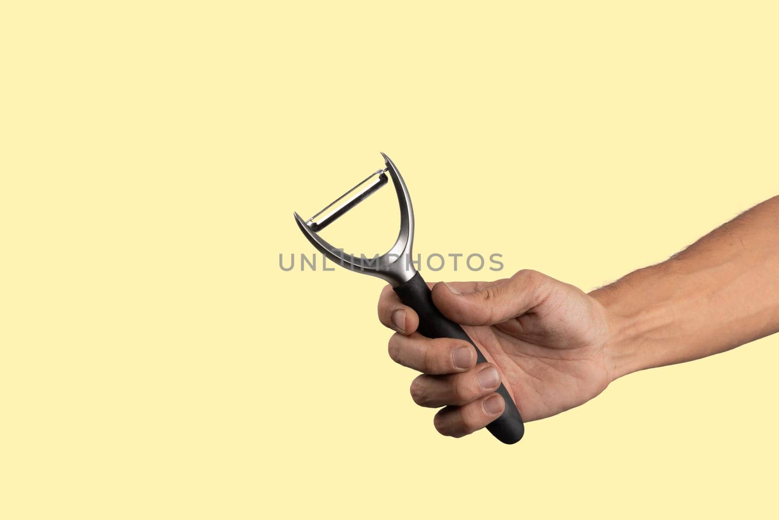 Black male hand holding a potato peeler isolated on yellow background. High quality photo
