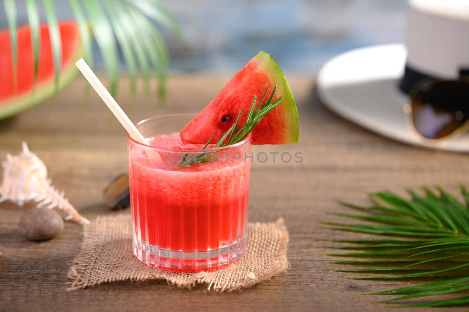Freshly watermelon juice in glasses and palm leaf on wooden table. Refreshing summer drink concept.