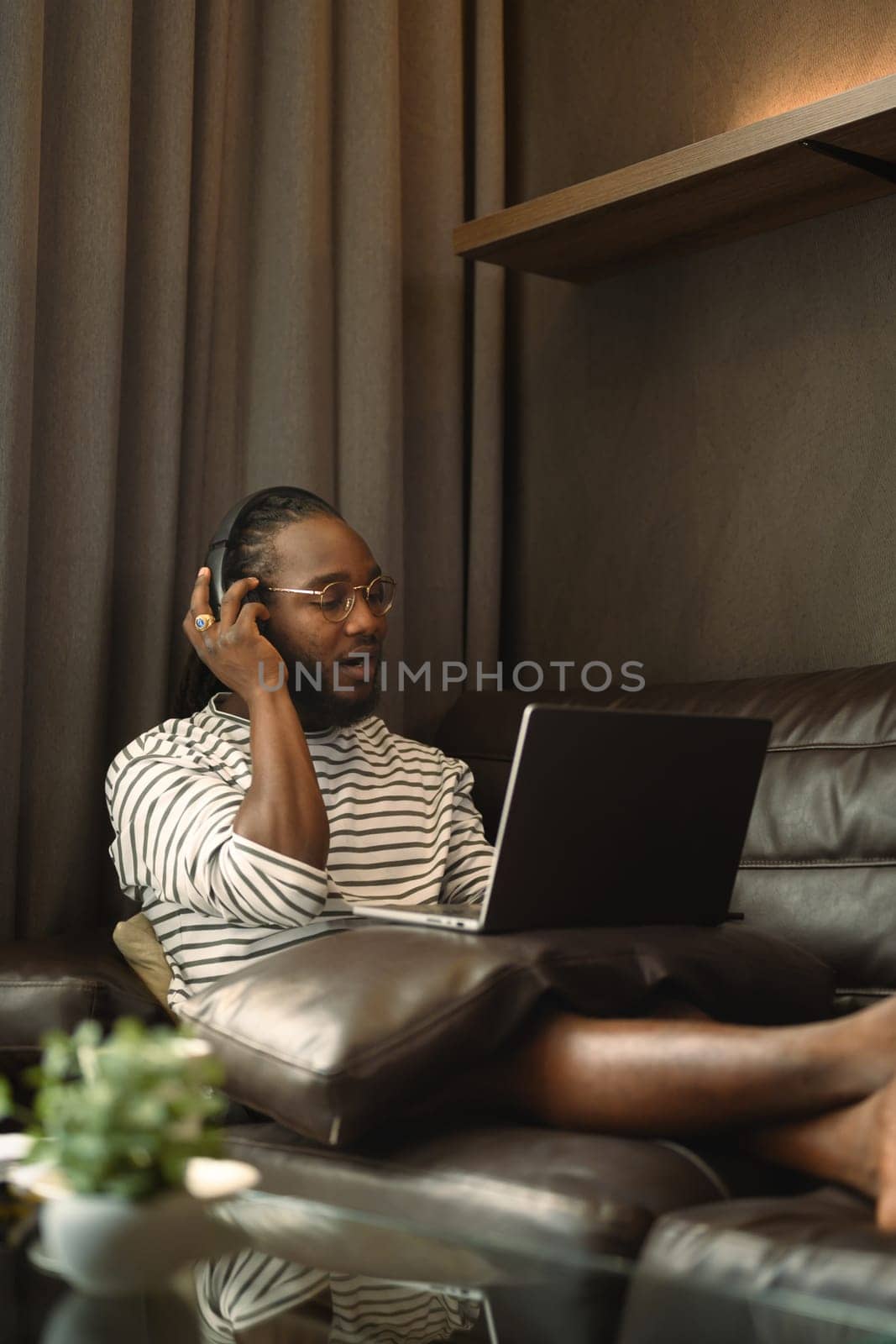 African man wearing headphone watching movie on laptop at home.