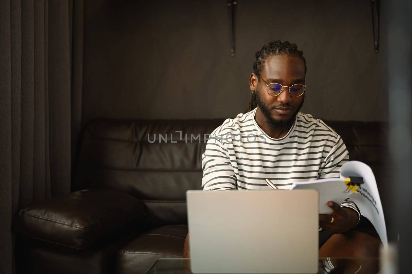 Focused male freelancer in eyeglasses checking financial report and using laptop on couch.