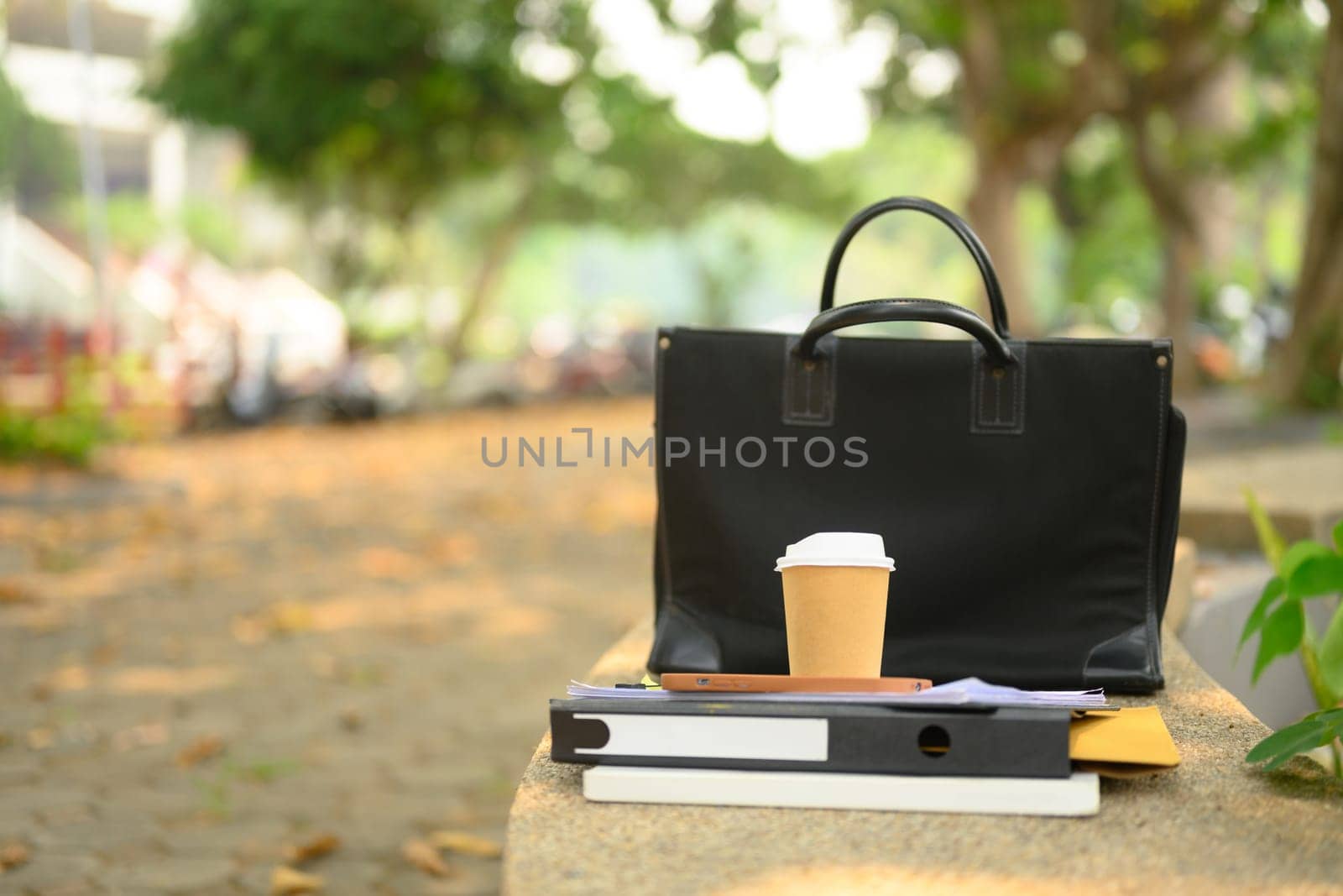 Closeup of briefcase, takeaway coffee cup and document on concrete bench. City life concept by prathanchorruangsak