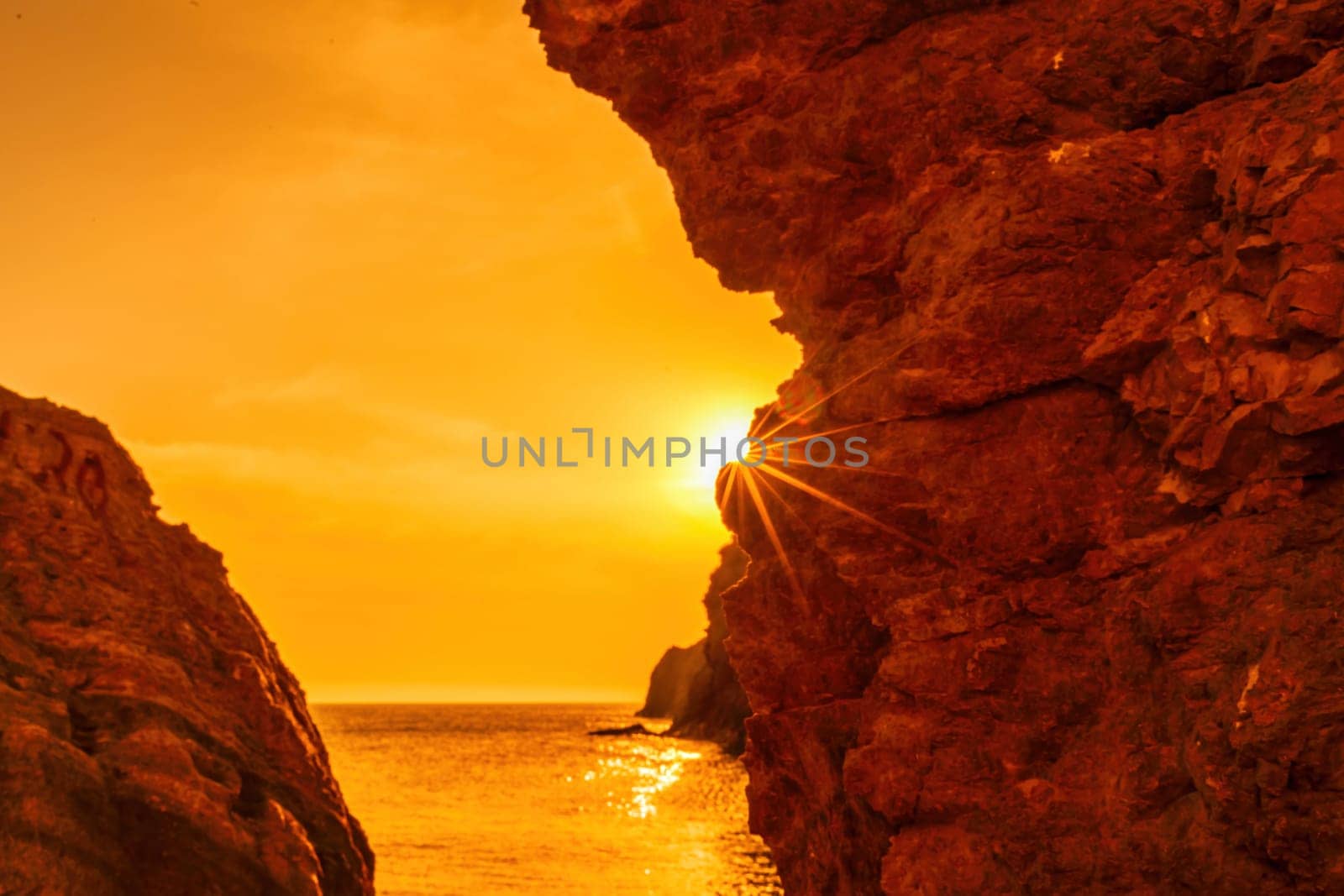 Woman tourist enjoying the sunset over the sea mountain landscape. Sits outdoors on a rock above the sea. She is wearing jeans and a blue hoodie. Healthy lifestyle, harmony and meditation.