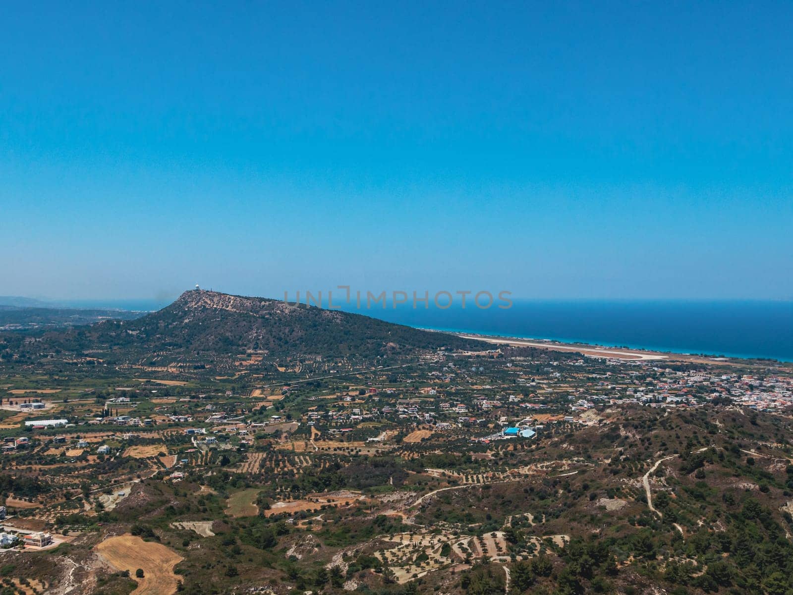 Beautiful panoramic view of a modern settlement along the coastline of the Aegean Sea around a low mountain in Greece on the island of Rhodes on a sunny summer day, side view from Mount Filerimos close up.