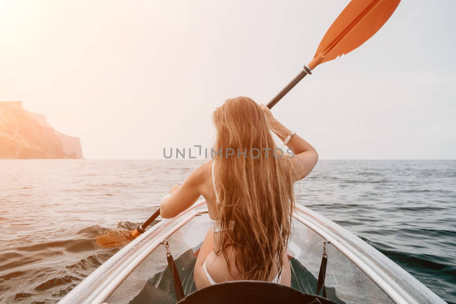 Woman in kayak back view. Happy young woman with long hair floating in transparent kayak on the crystal clear sea. Summer holiday vacation and cheerful female people relaxing having fun on the boat by panophotograph