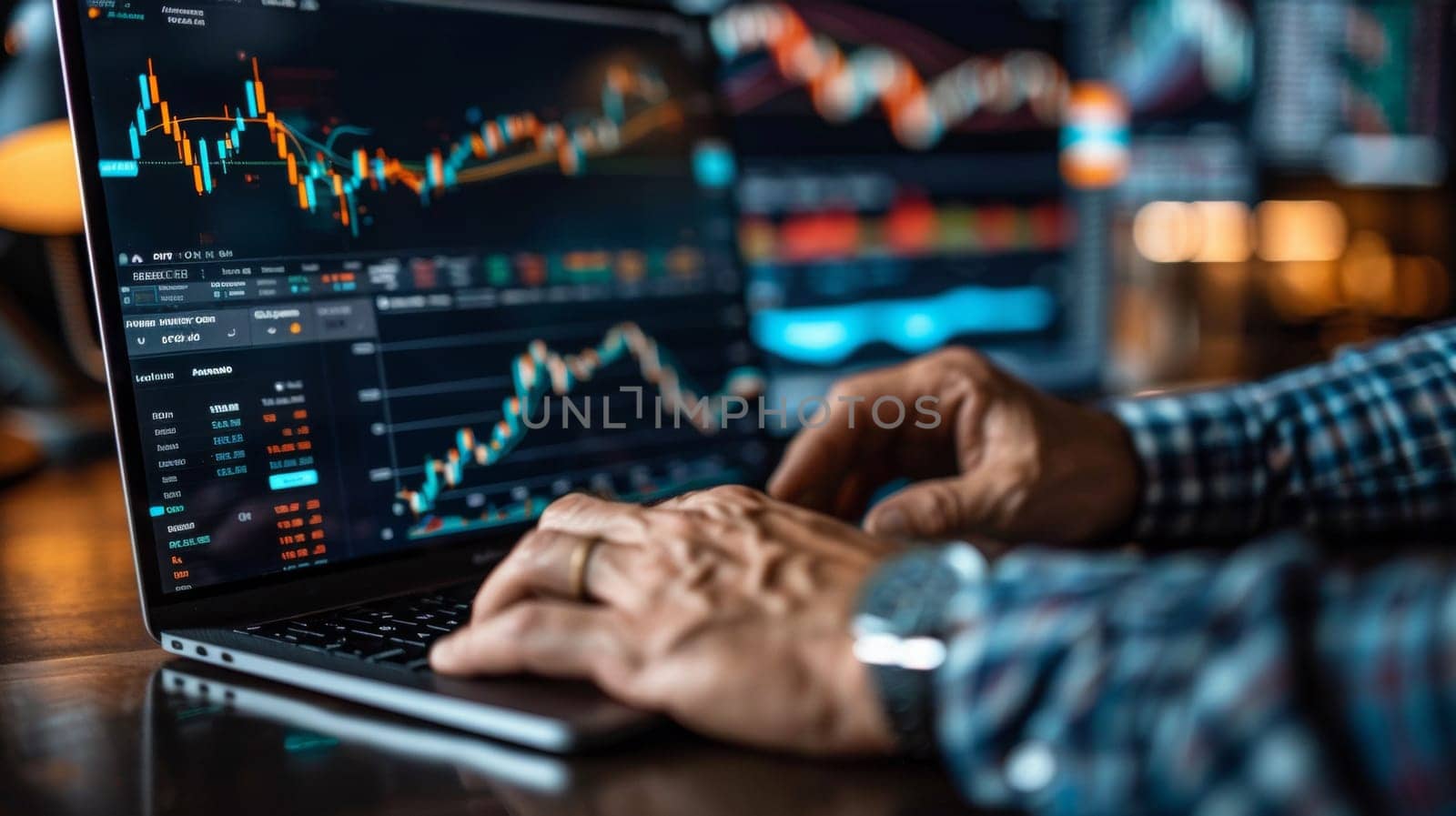 A person is typing on a laptop with stock market graphs
