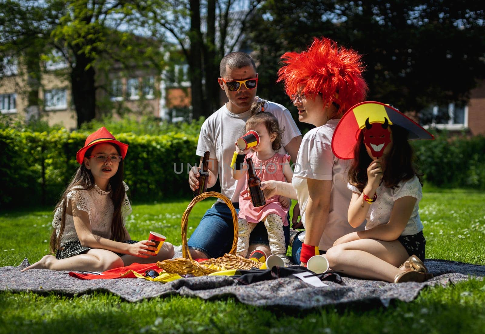 Portrait of beautiful and happy caucasian parents with three kids girls, drinks in their hands, celebrating Belgian day at a picnic in a city park on a sunny summer day, close-up top view.