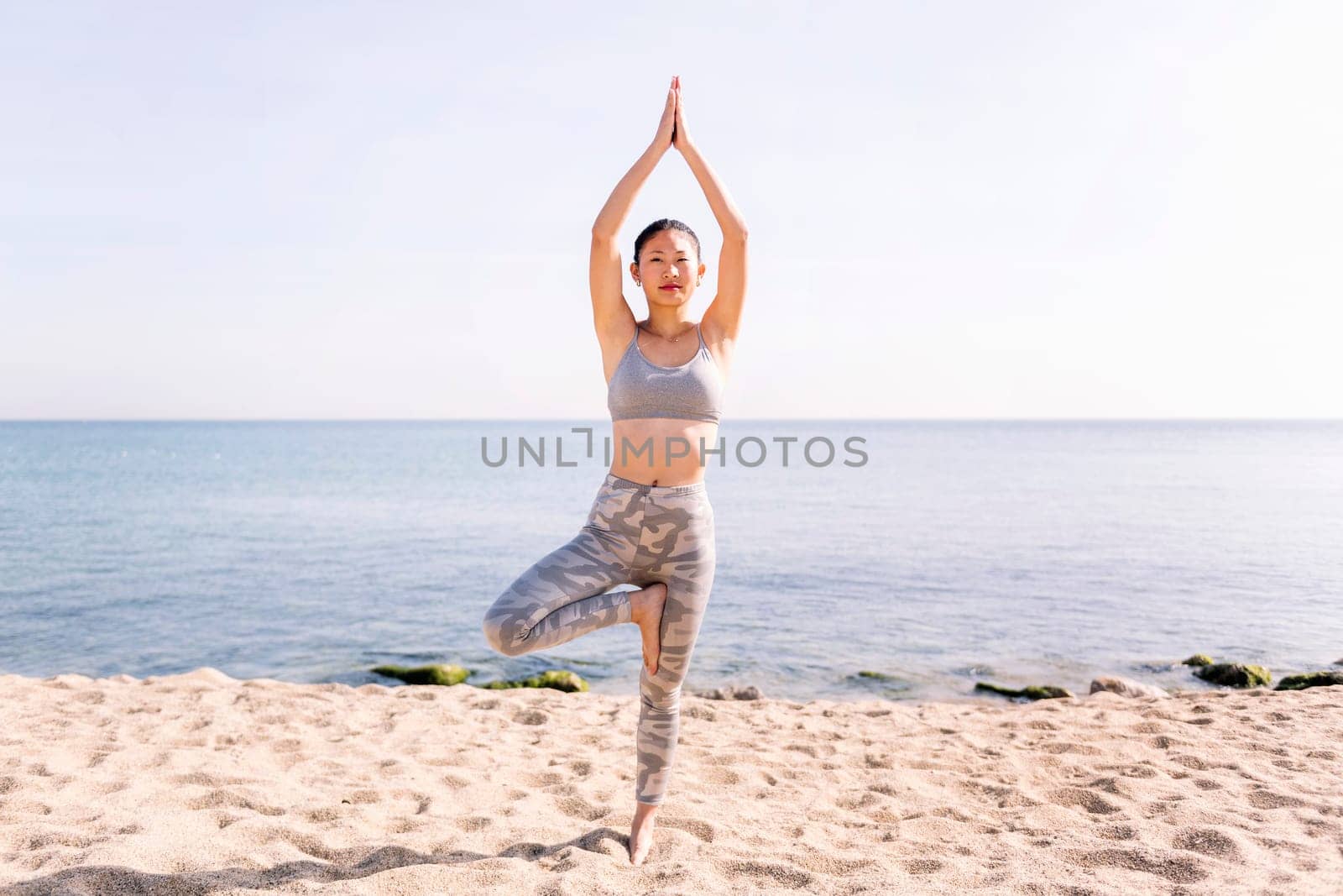young woman doing yoga tree position at beach by raulmelldo