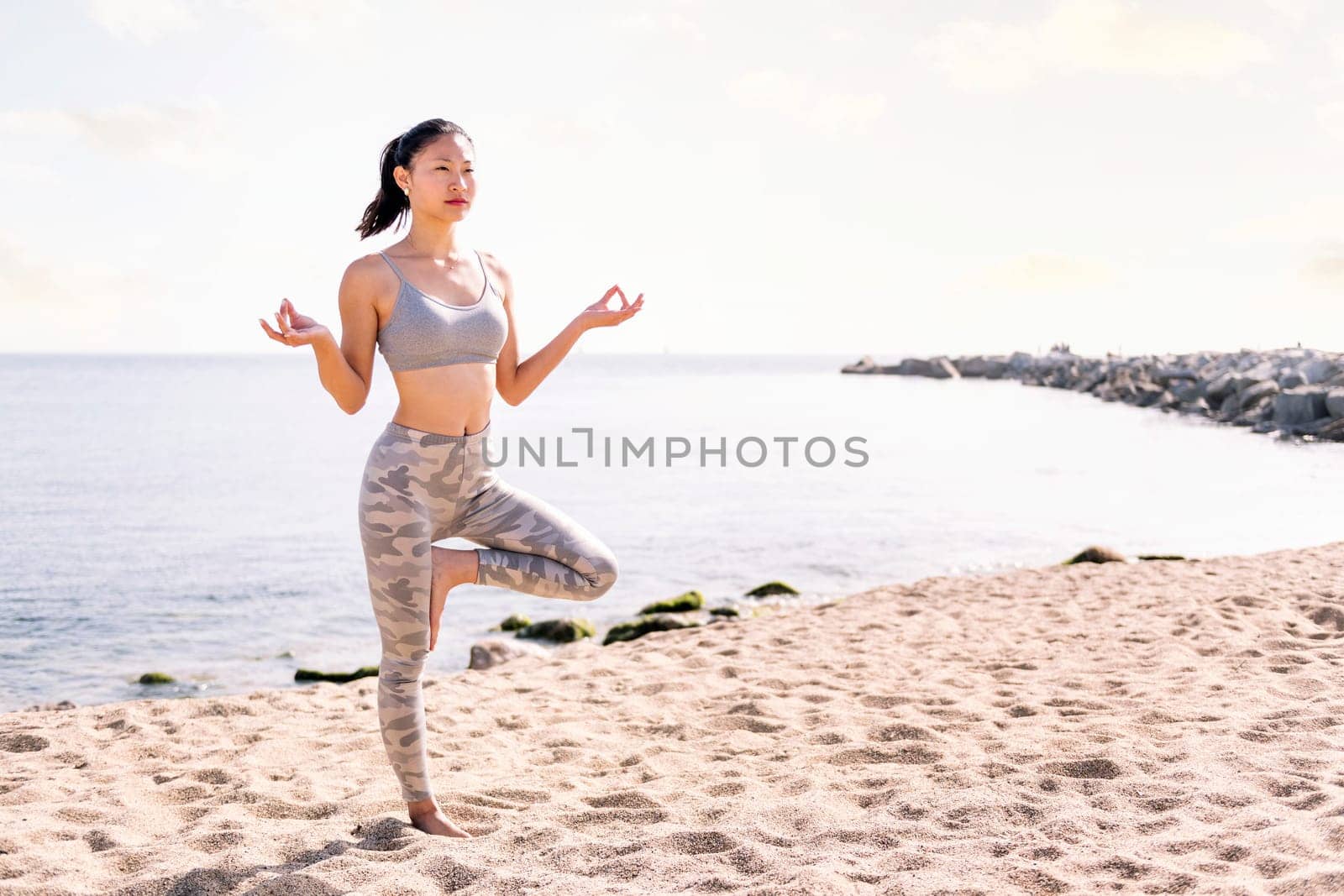 young asian woman in sportswear doing yoga position at beach, concept of mental relaxation and healthy lifestyle