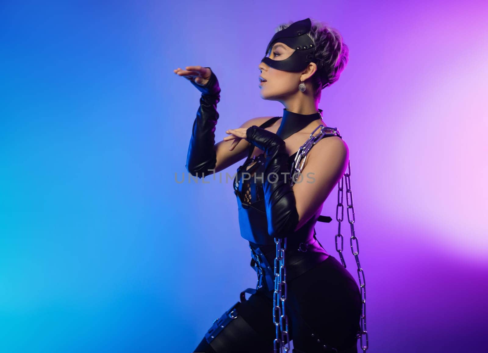 sexy girl in the erotic image of a catwoman in leather belts and a mask poses against the background of a copy paste in a beautiful neon background with a metal chain in her hands by Rotozey