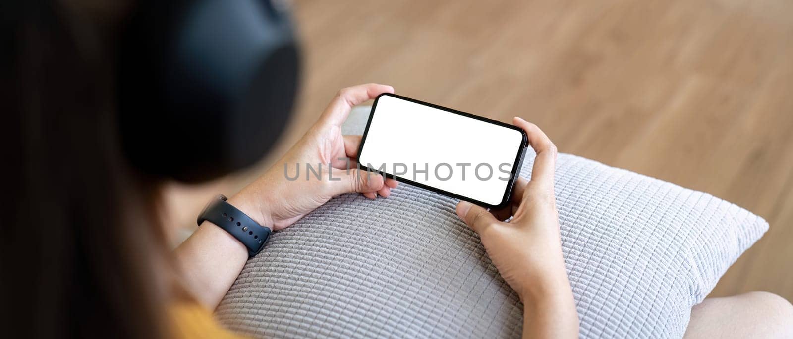 Mockup smartphone of a woman holding mobile phone with blank white screen while sitting listen to music at home.