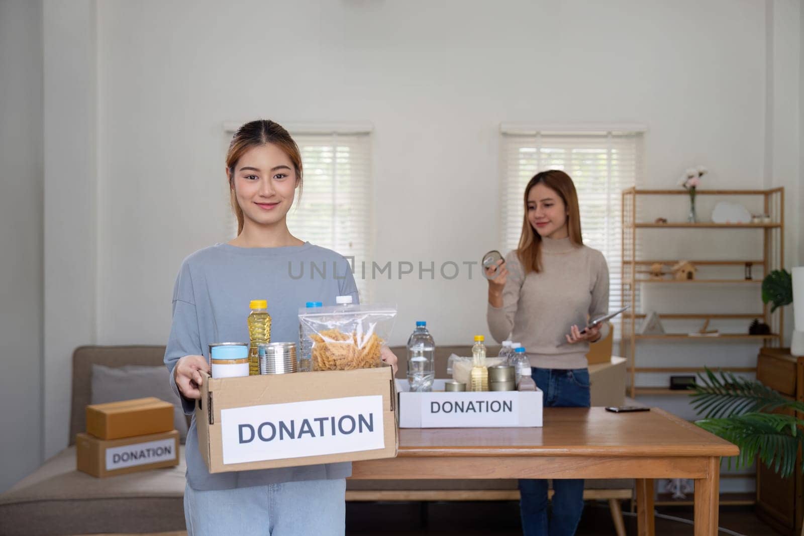 Donation and two woman volunteer asian of happy packing food in box at home. Charity by nateemee