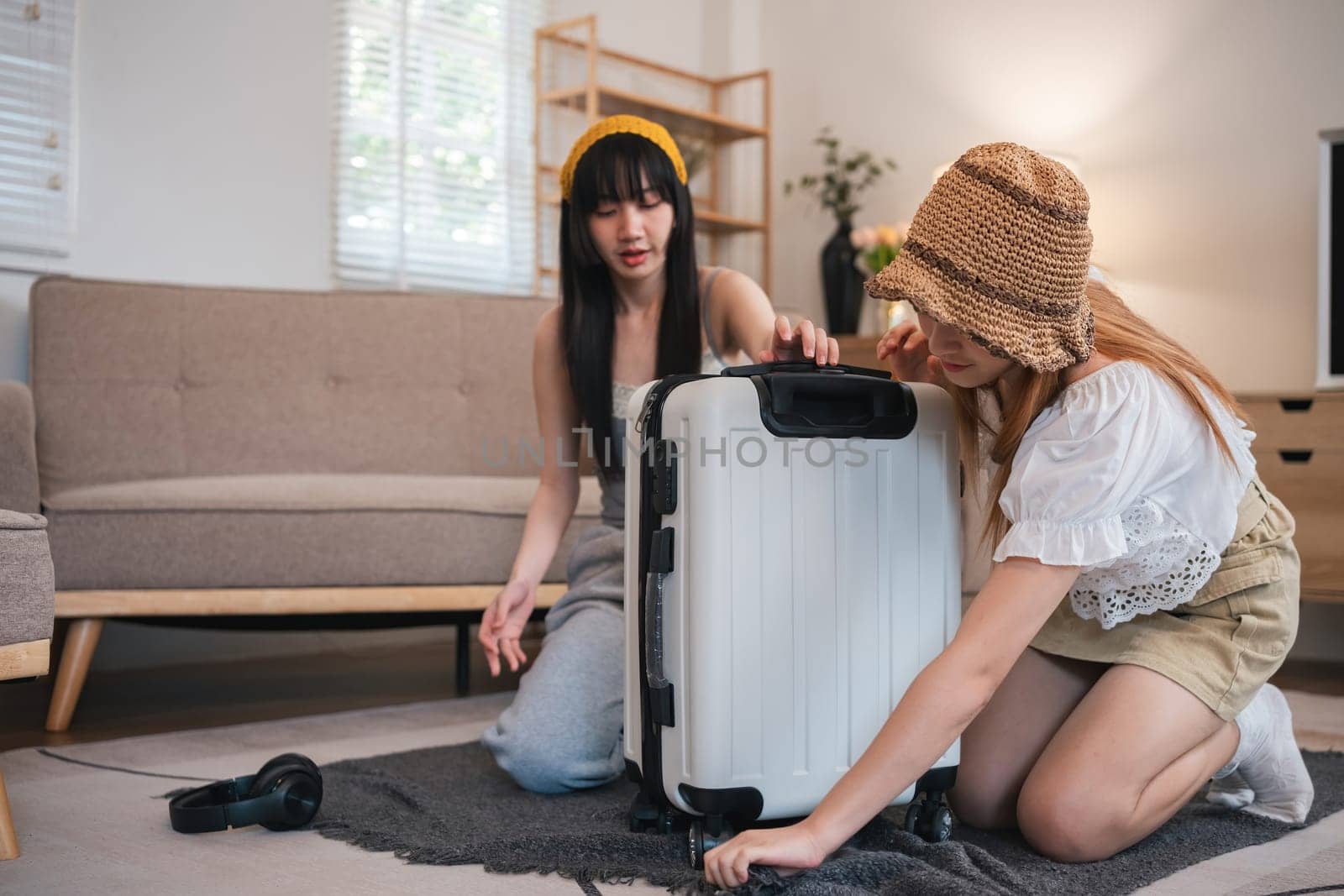 Two young female friends pack a suitcase with clothes and travel passports in preparation for a weekend away. by wichayada