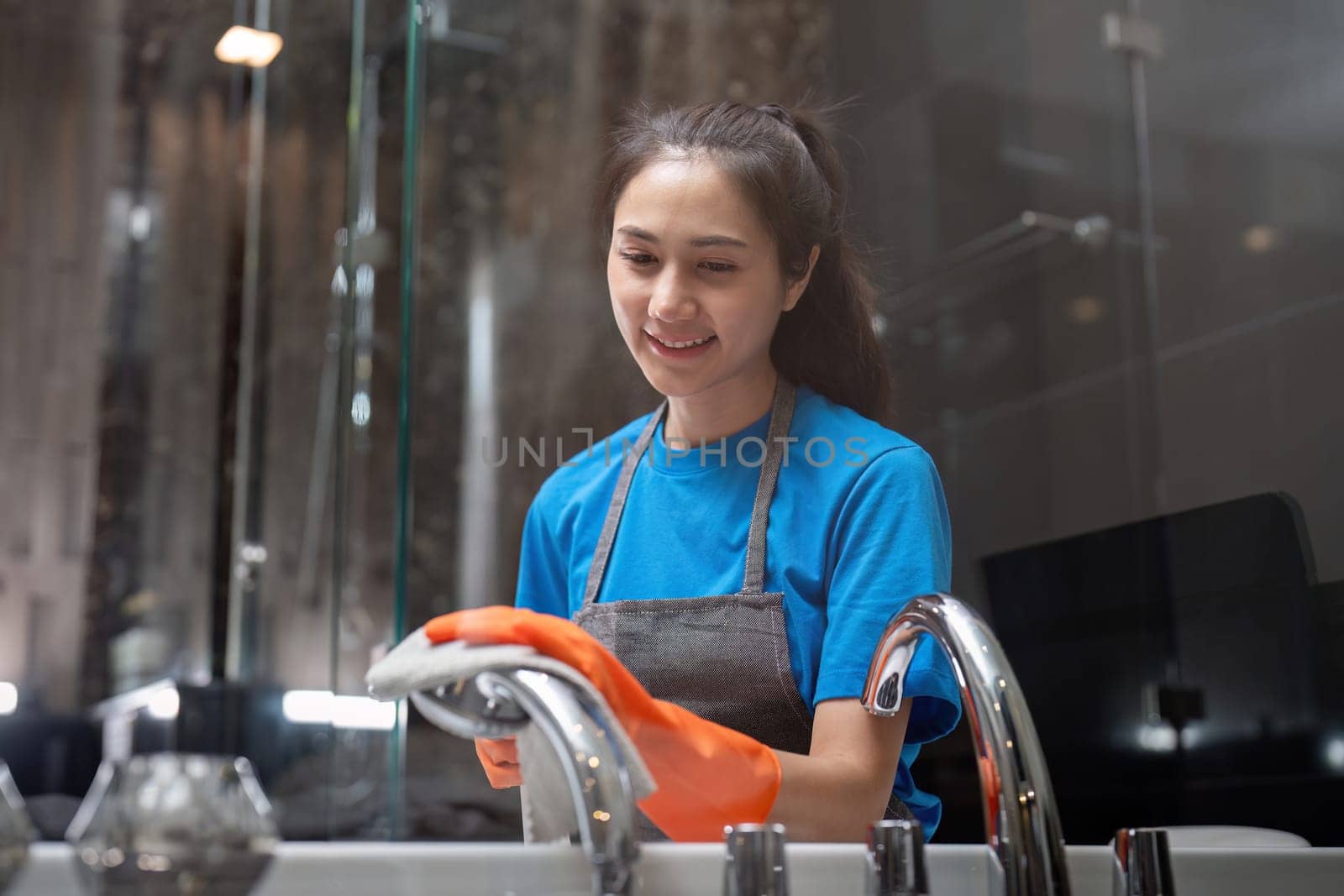 Professional cleaning service company employee in rubber gloves cleaning and detergent spray in bathroom.