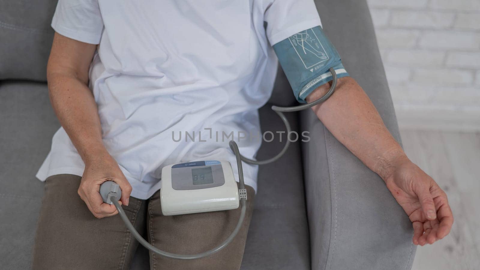 Mature Caucasian woman measuring blood pressure while sitting on sofa at home