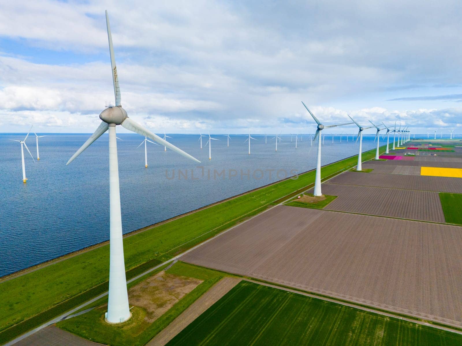 A mesmerizing aerial view of a wind farm near the ocean, where giant turbine blades spin gracefully against the backdrop of the water by fokkebok