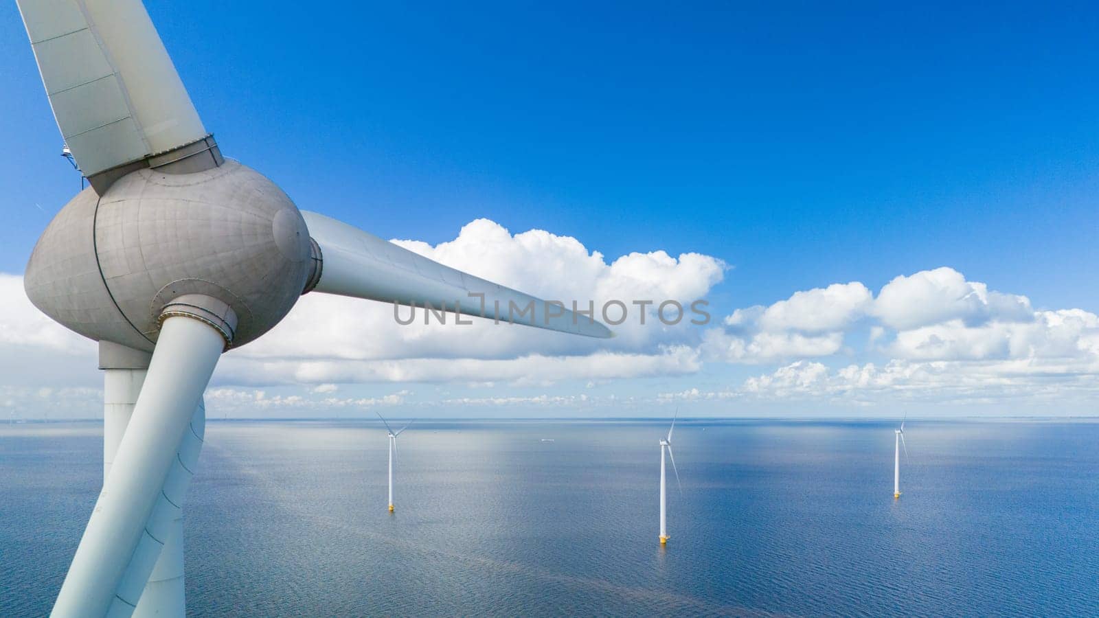 A single wind turbine stands tall in the middle of the vast ocean, harnessing renewable energy while surrounded by an endless expanse of water under a clear blue sky in the Noordoostpolder Netherlands