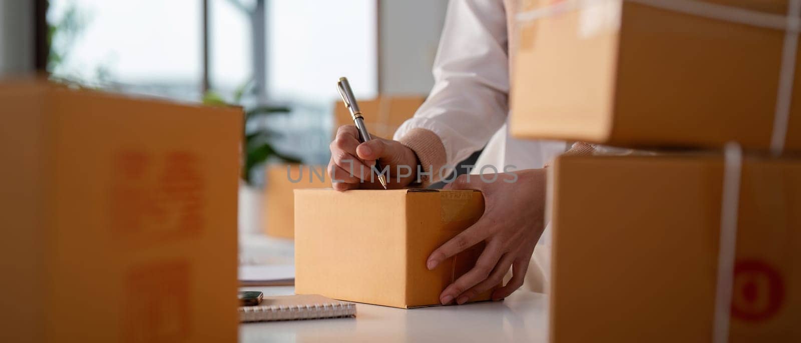 Woman entrepreneur prepare parcel box and check online order on laptop computer for commercial checking delivery. online marketing, packing box, SME seller. startup business concept by nateemee