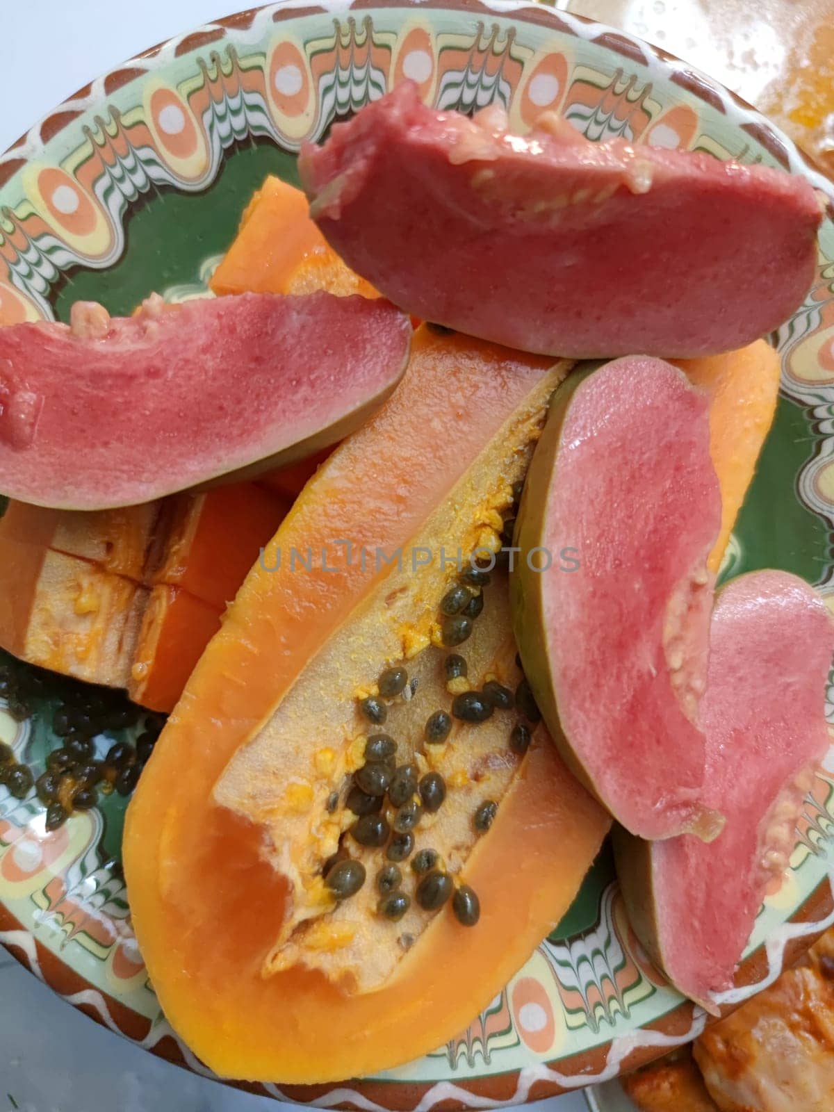 sliced papaya and guava on a patterned ceramic plate by Annado