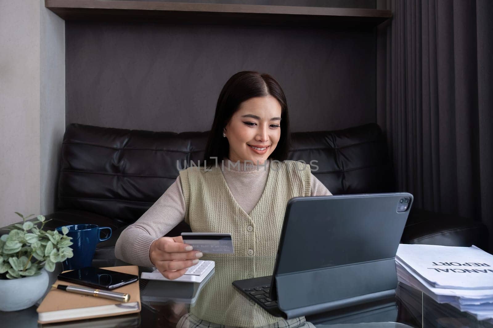 Beautiful young woman uses laptop to shop online Buy things from home and pay by credit card through the online banking app by phone.