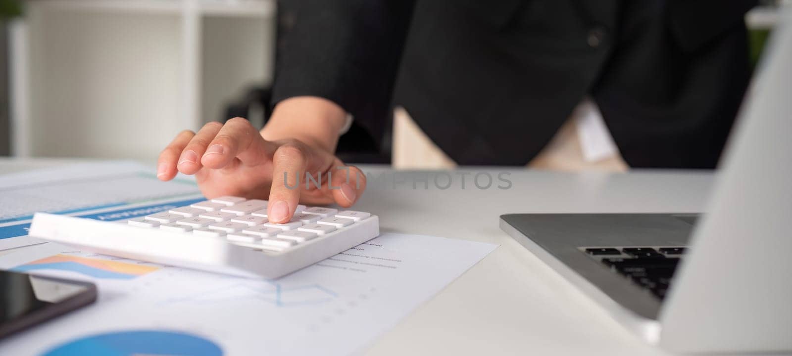 Asian female accountant Use a calculator to calculate business numbers on a white wooden table in the office. by wichayada