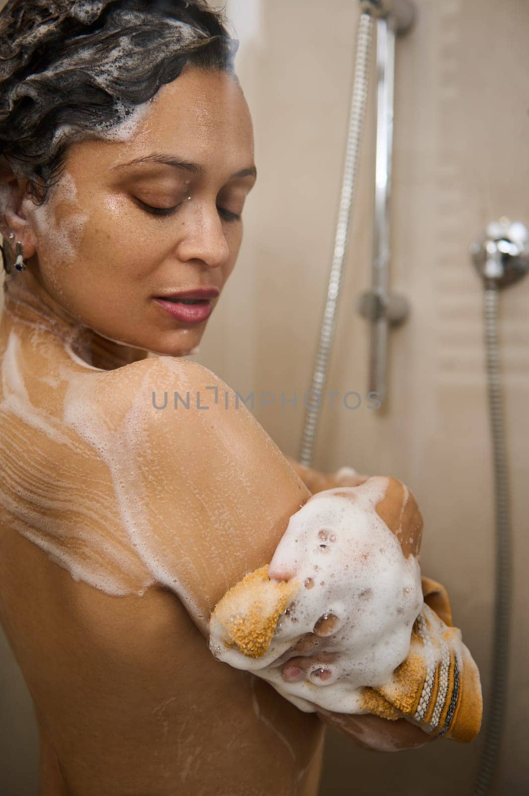 Beautiful sexy young woman washing her body with moisturizing gel, standing under splashing water jet, relaxing enjoying her bathing in the bathroom douche cabin. Happy woman relaxing in shower stall