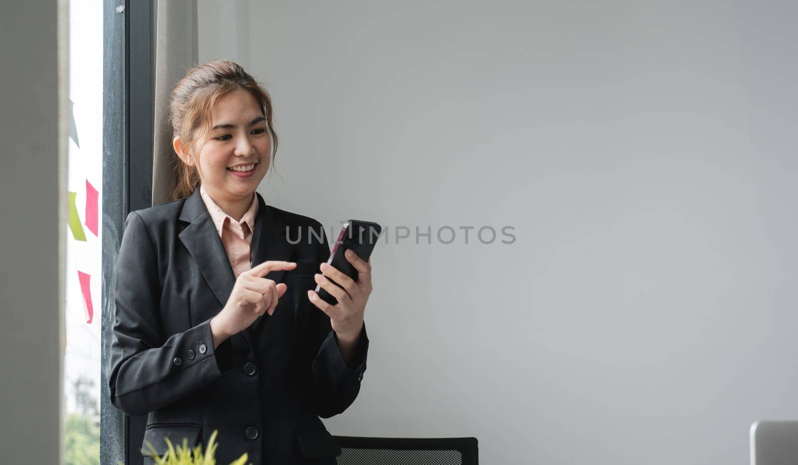 Beautiful business woman in the office, happy and smiling business woman uses internet phone close up, female worker reads message and browses internet pages inside office building.