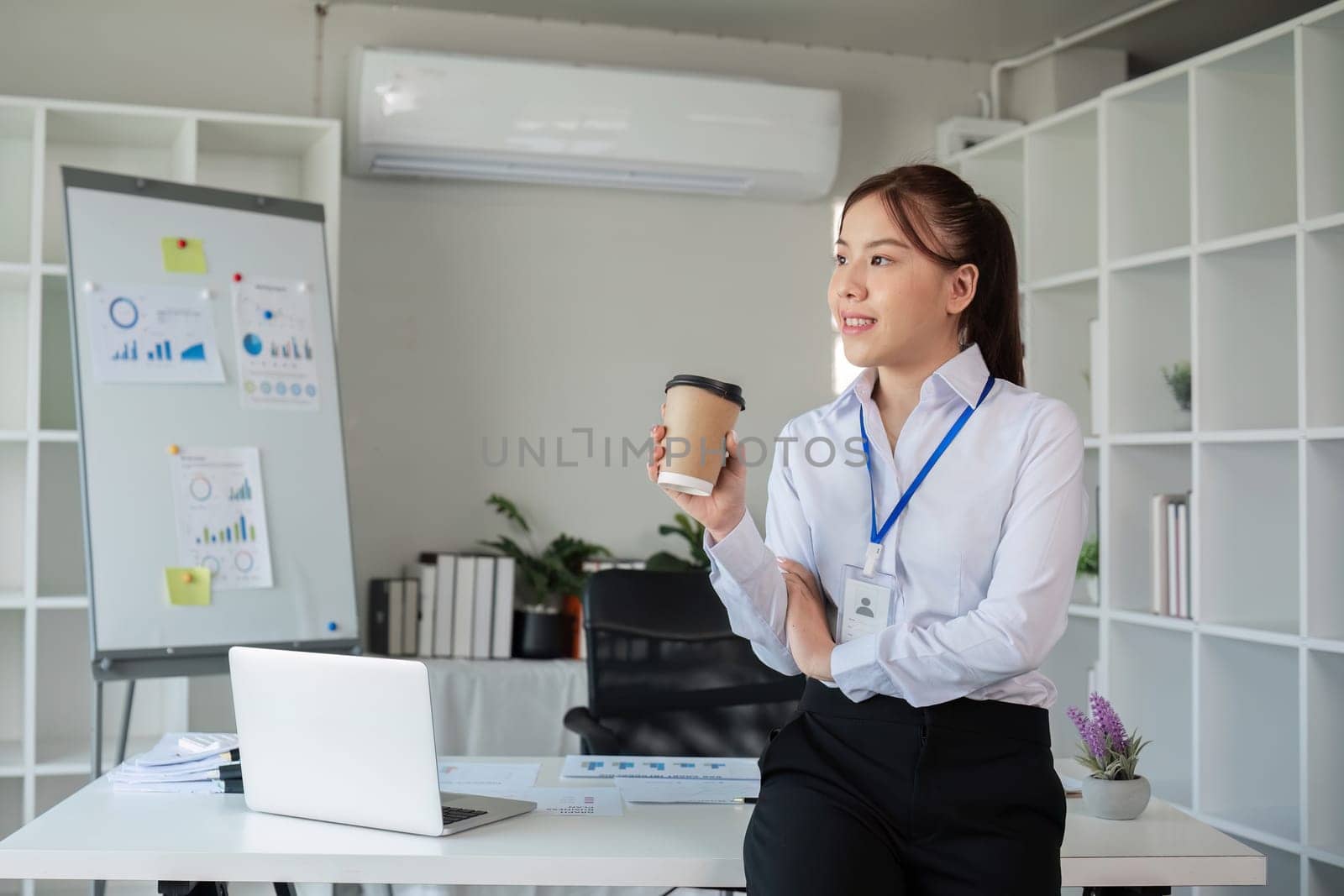 Portrait of a confident young Asian business woman standing at a desk in the office. by wichayada