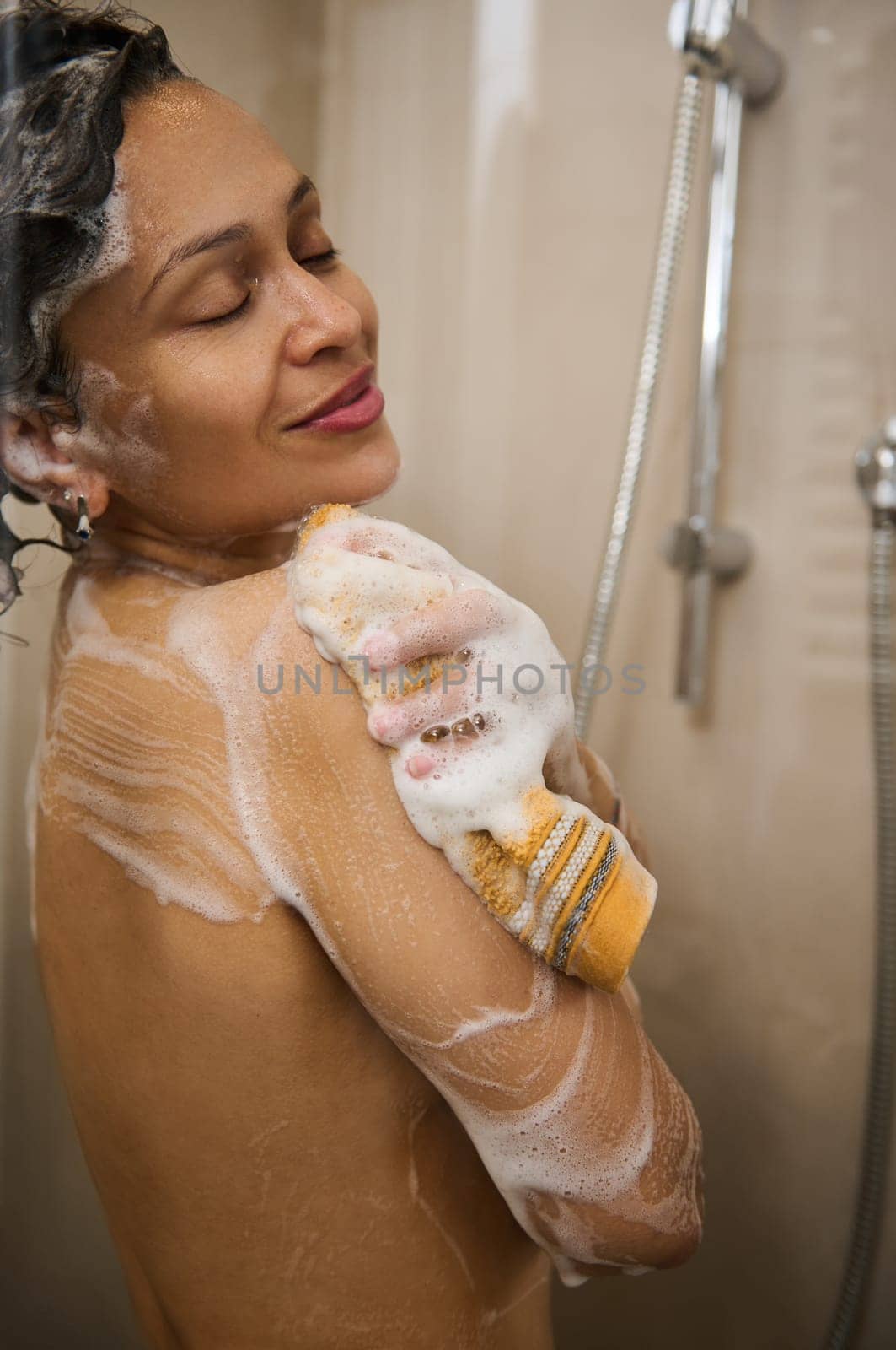 Attractive sexy woman smiles and enjoys a shower with foam, in a douche cabin in her bathroom. Home spa, beauty, nudity, relaxation, skin, body and hair care. Morning daily routine. Purity and hygiene