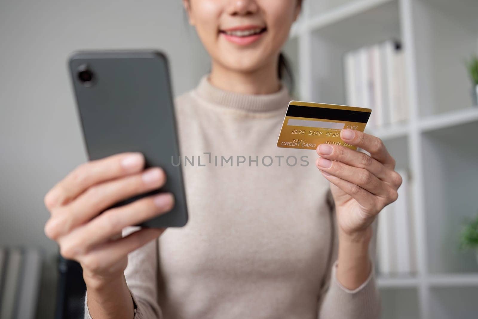 Beautiful young woman uses laptop to shop online, buys things and pays with credit card through phone online banking app..