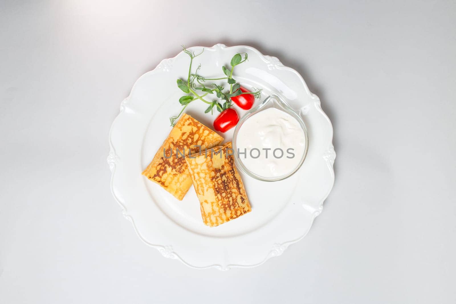 Top view of Pancakes with sour cream and cherry tomatoes on a white background. Carnival menu.