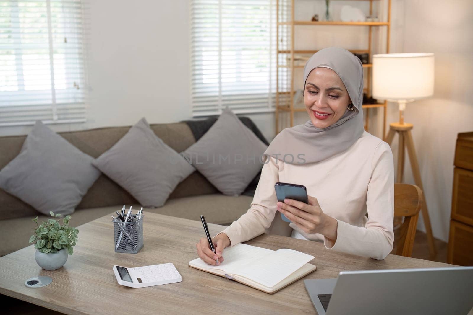 Young muslim business woman calculate budget money finance. Muslim woman accountant use calculator typing laptop counting tax loan bills online payment write document paperwork at home office.