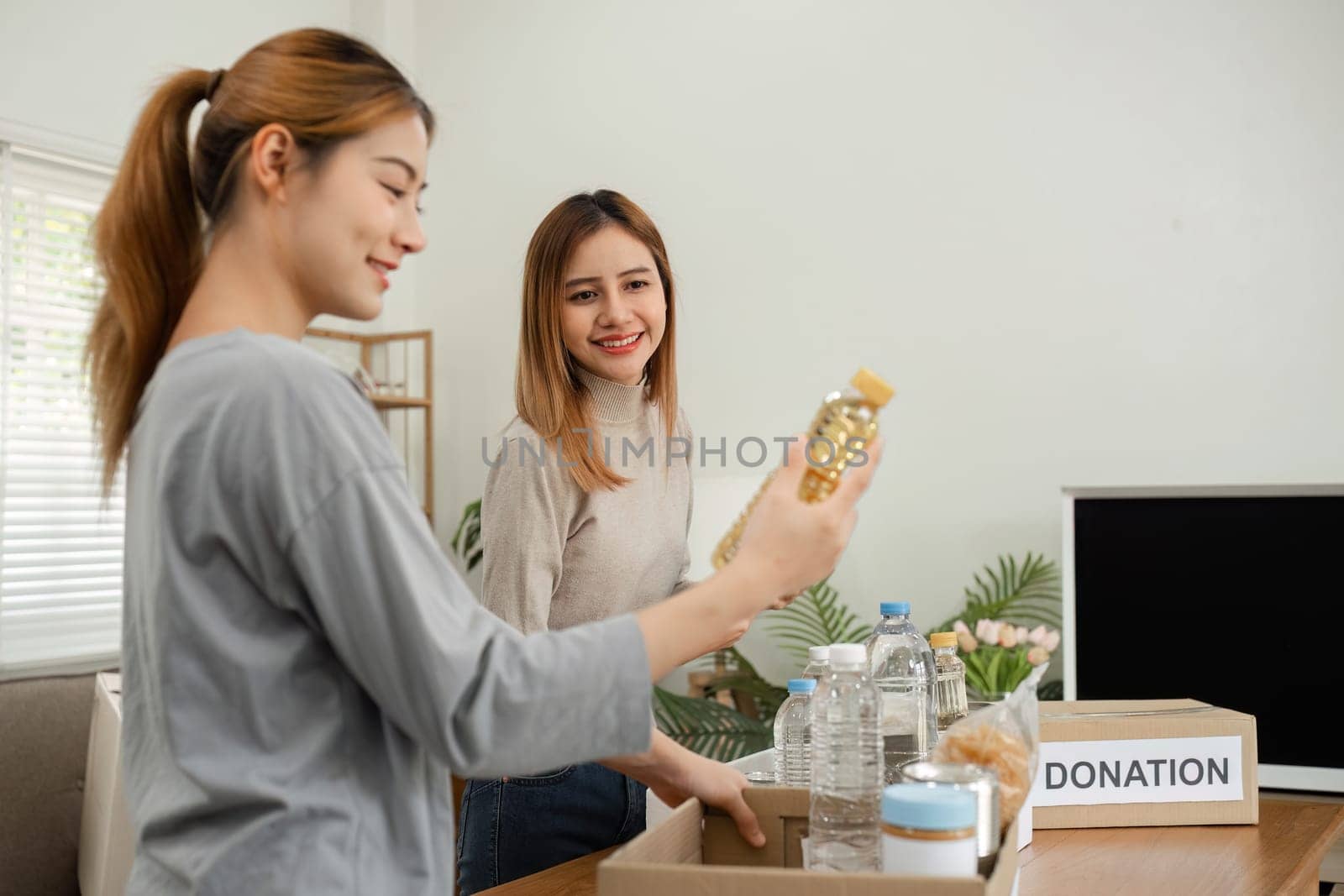 Two young female volunteers help pack food into donation boxes and prepare to donate them to charity..