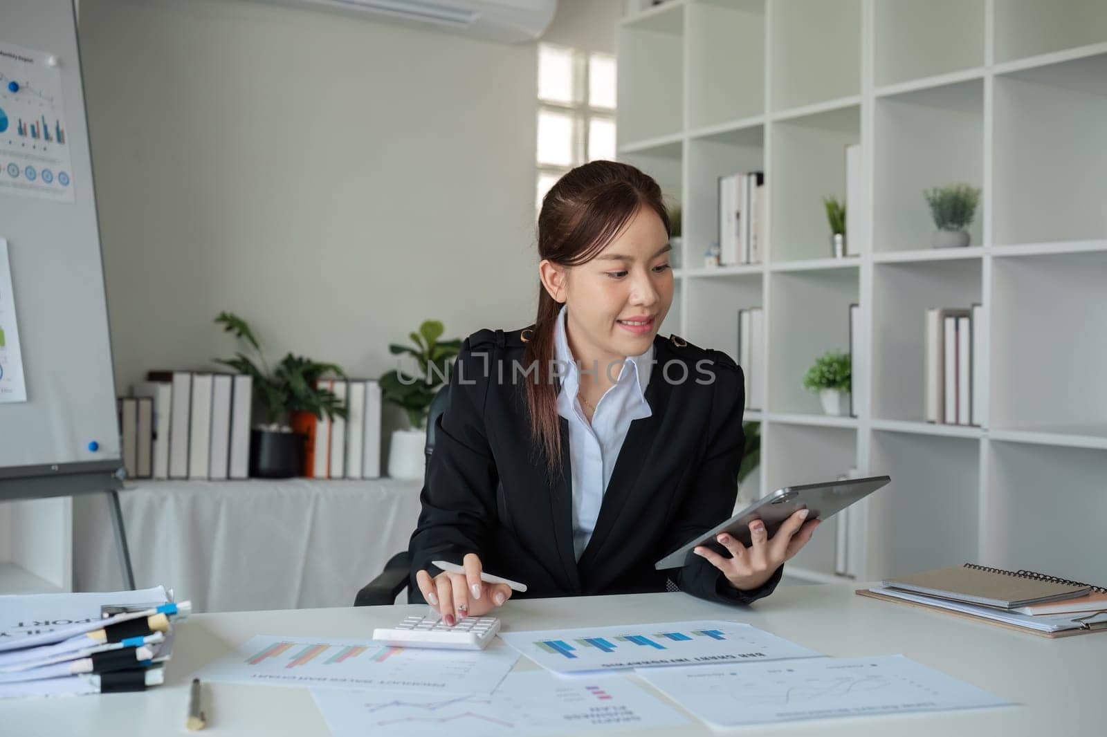 Young woman accountant uses calculator to calculate finances or graph business numbers on white wooden table in office. by wichayada