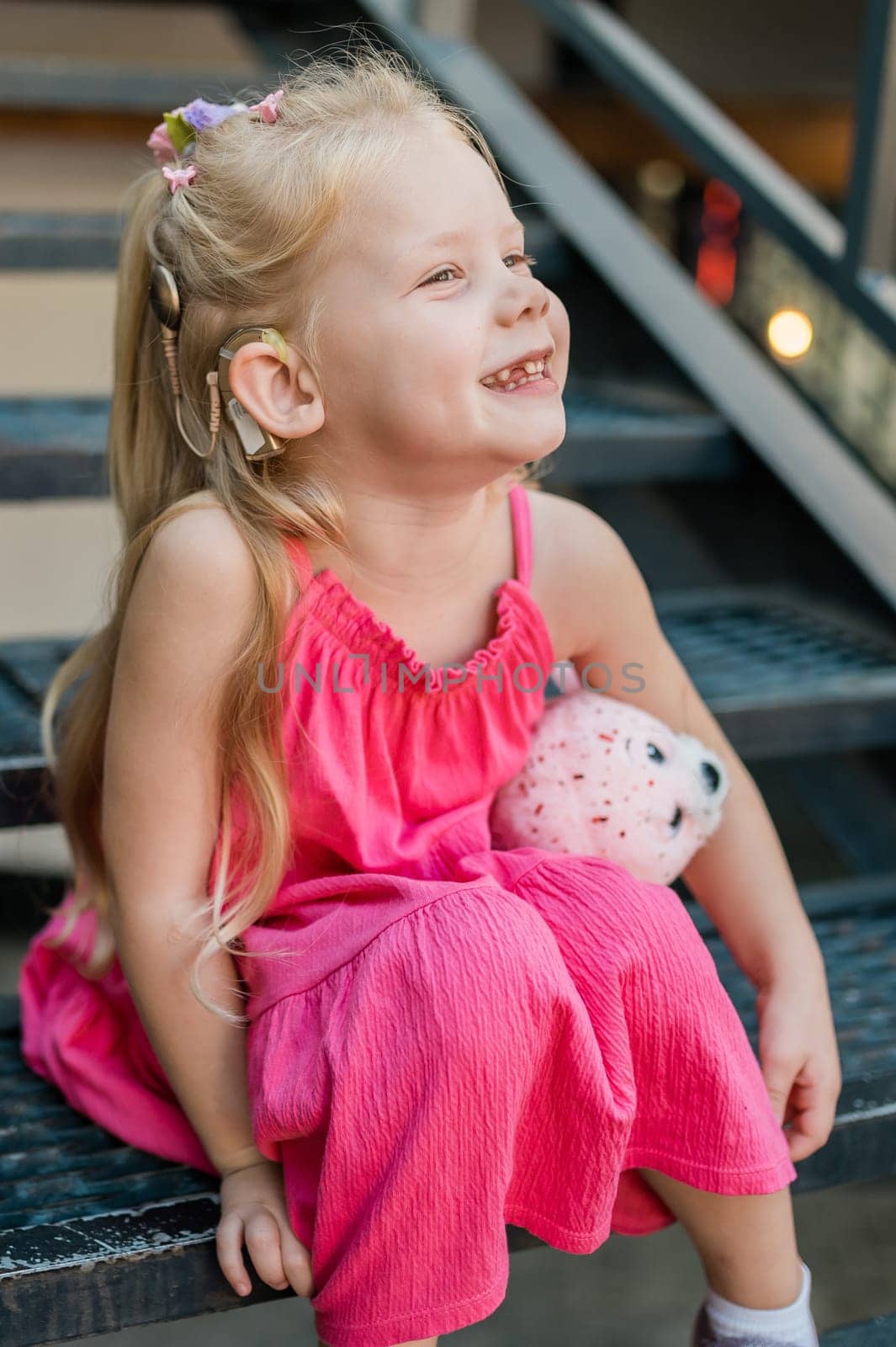 Child girl walks and have fun outdoor with cochlear implant on the head. Hearing aid and treatment concept. Copy space vertical.