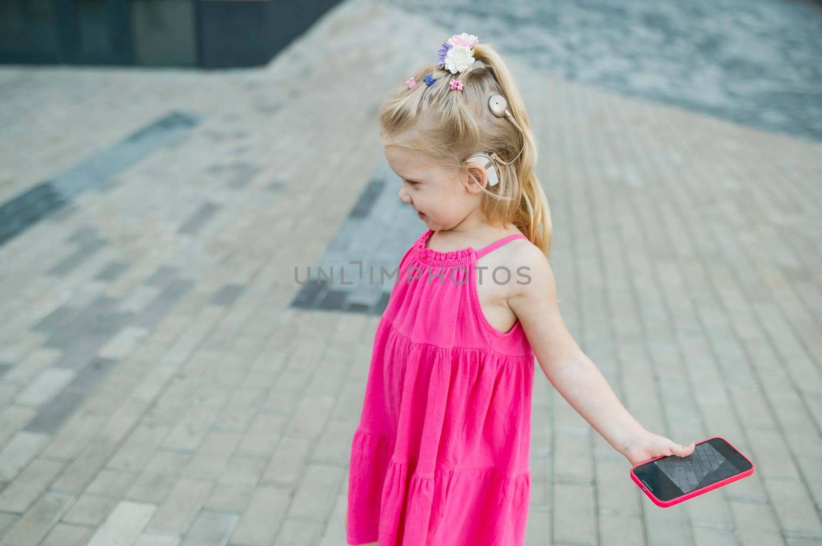 Child girl walks and have fun outdoor with cochlear implant on the head. Hearing aid and treatment concept. Copy space vertical.