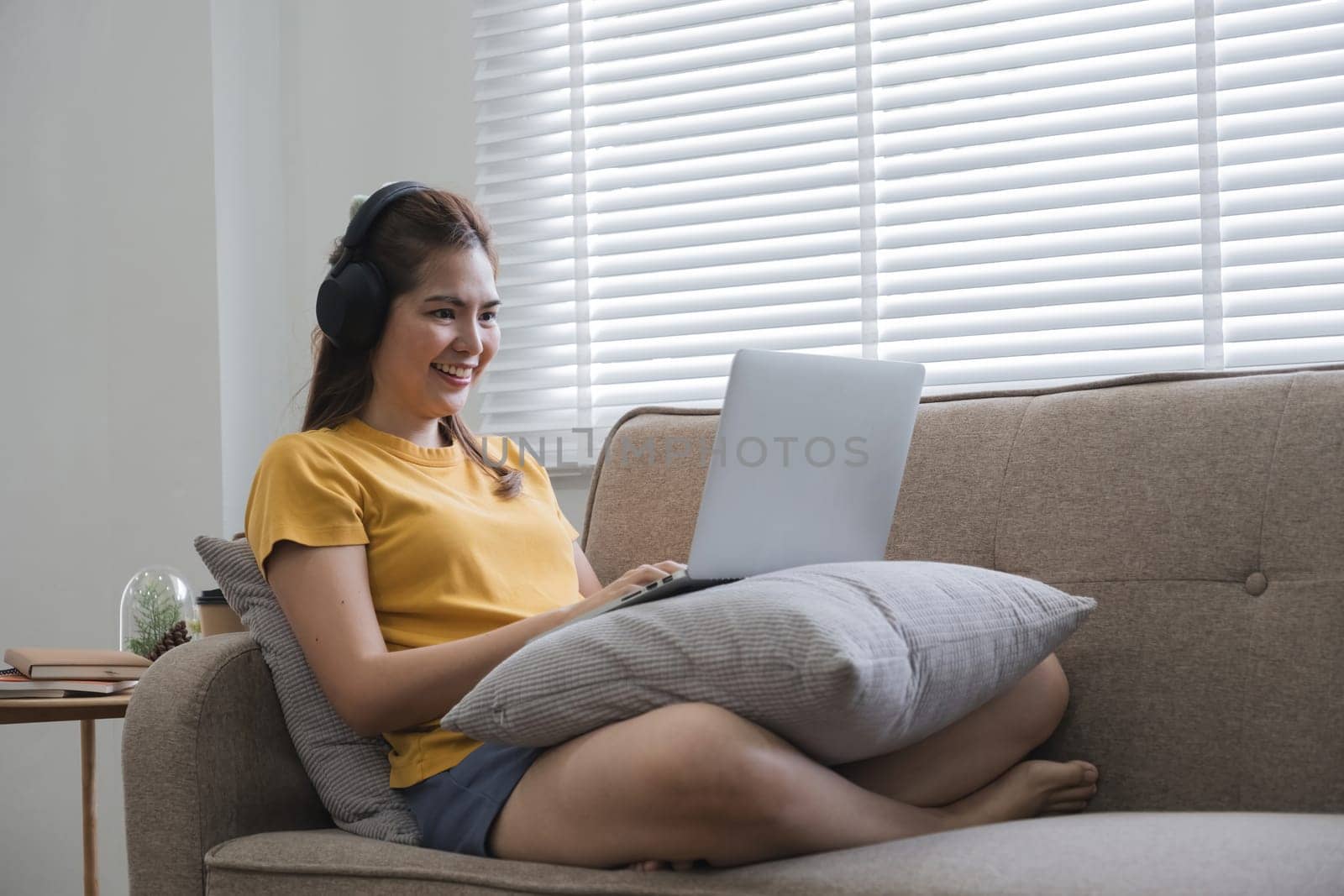 A woman is sitting on a couch with a laptop in front of her.