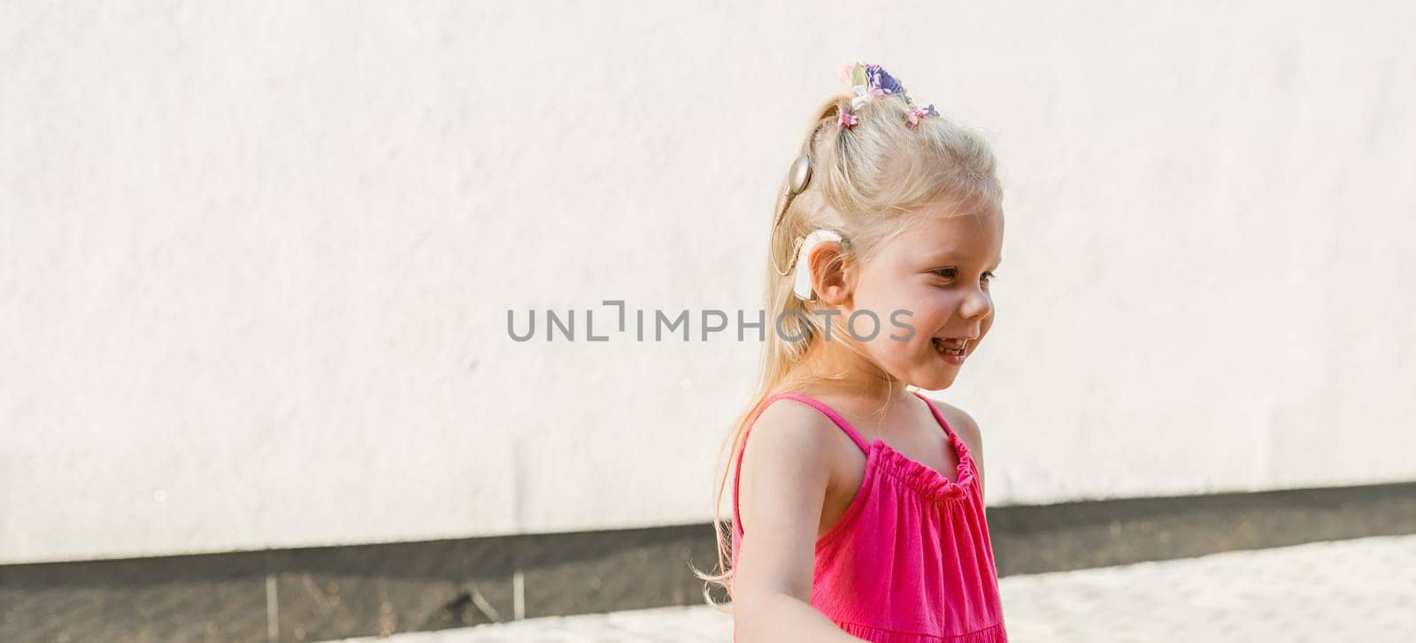 Child girl walks and have fun outdoor with cochlear implant on the head. Hearing aid and treatment concept. Copy space vertical.