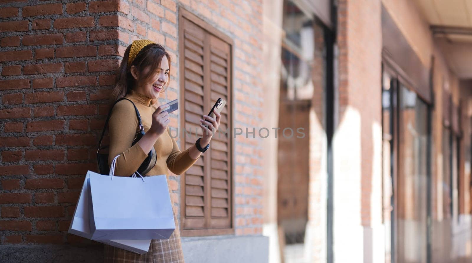 Asian woman shopping on the phone Looking at credit card with white shopping bag.